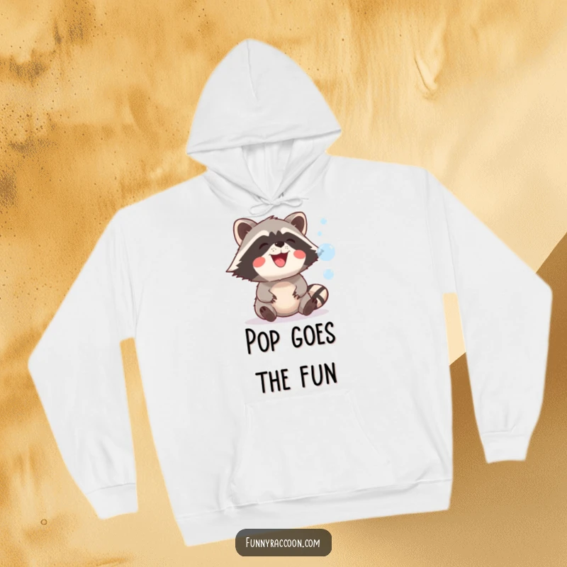 A cozy hoodie featuring a funny raccoon with a wide, happy grin trying to catch shimmering bubbles in a playful outdoor scene.